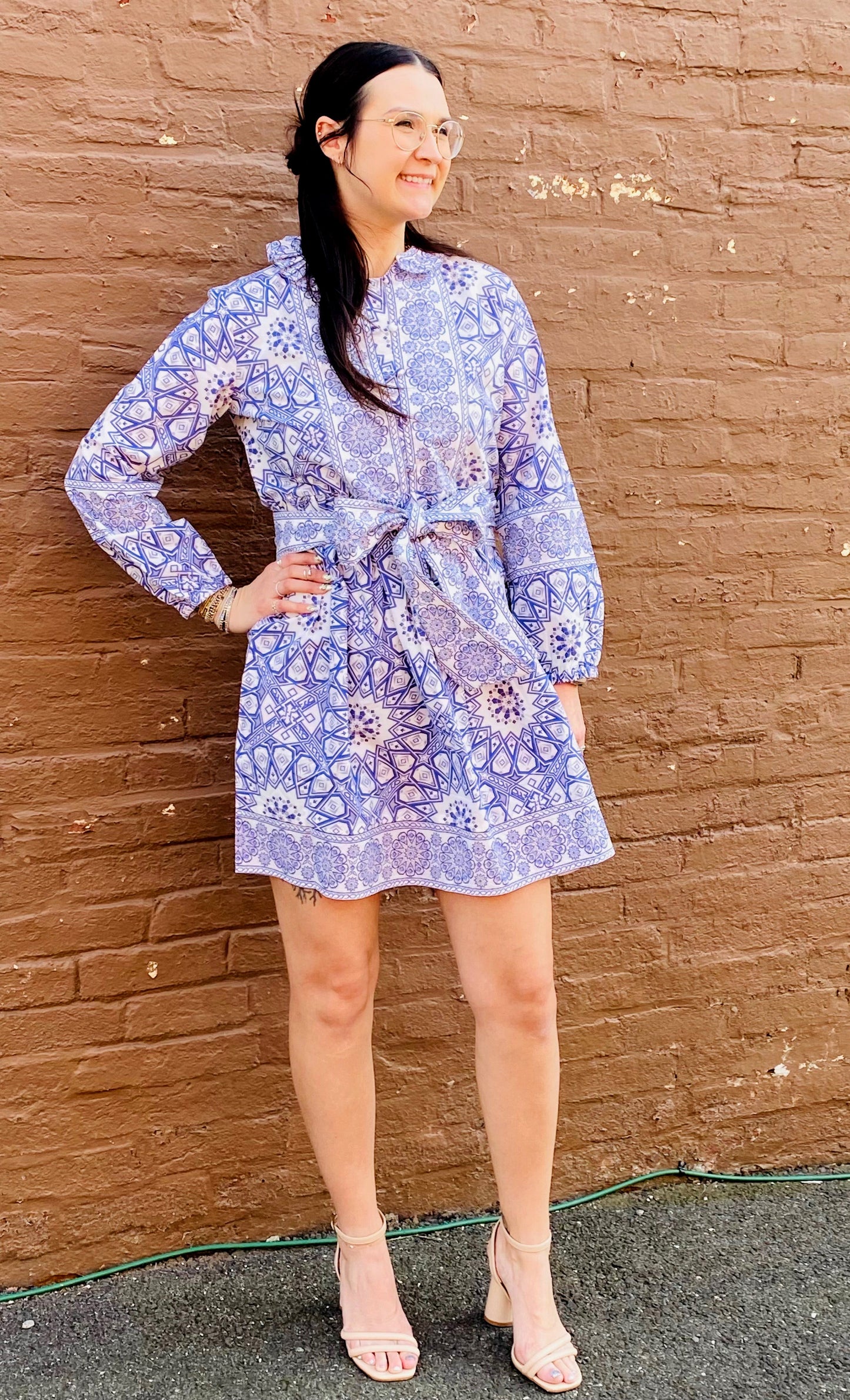 Woman wearing a blue floral dress standing against a brown brick wall.