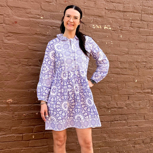 Woman wearing a light purple floral dress against a brown brick wall.