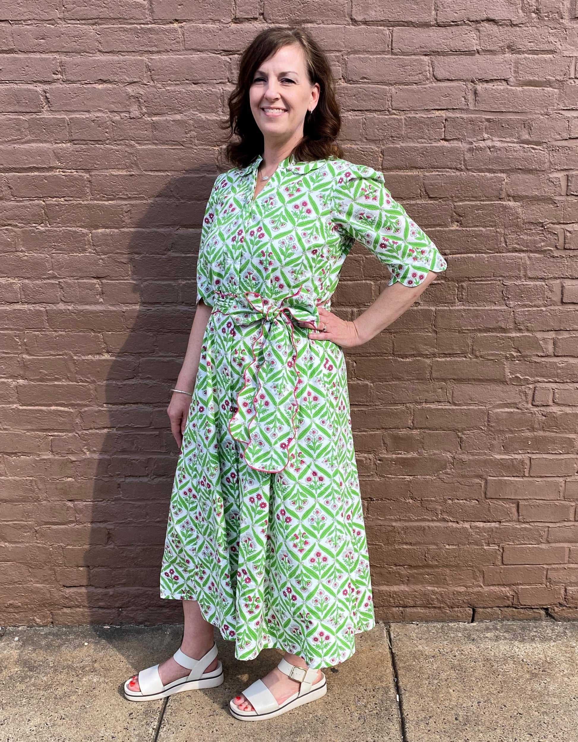 Woman wearing a green patterned dress standing against a brick wall.
