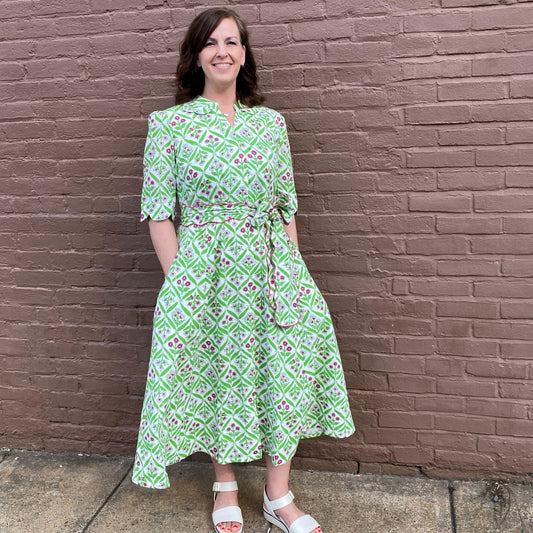 Woman wearing a green patterned dress standing against a brick wall.